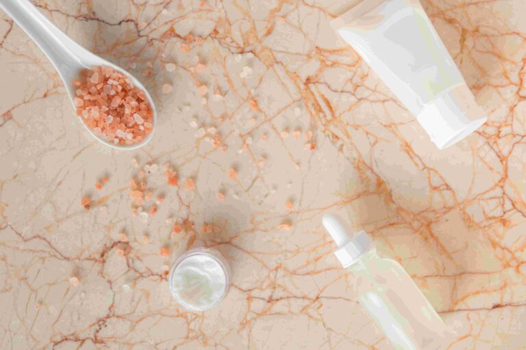 מוצרי טיפוח וספא על משטח שיש: מלח אמבט בתוך כף, קרם פנים ובקבוק סרום עם טפטפת